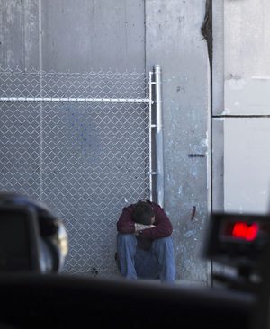 A homeless man sits outside of the Gospel Mission away from others.