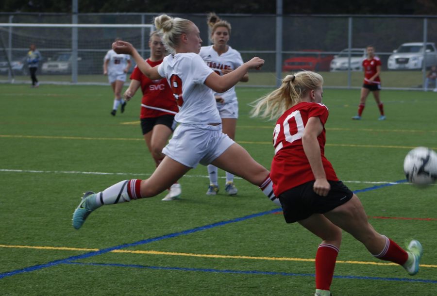 Camryn Cross (left, in white) lunges for the ball as her opponent in red kicks it.