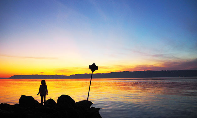 A child on Mukilteo Beach watching as the sun sets over Whidbey Island.