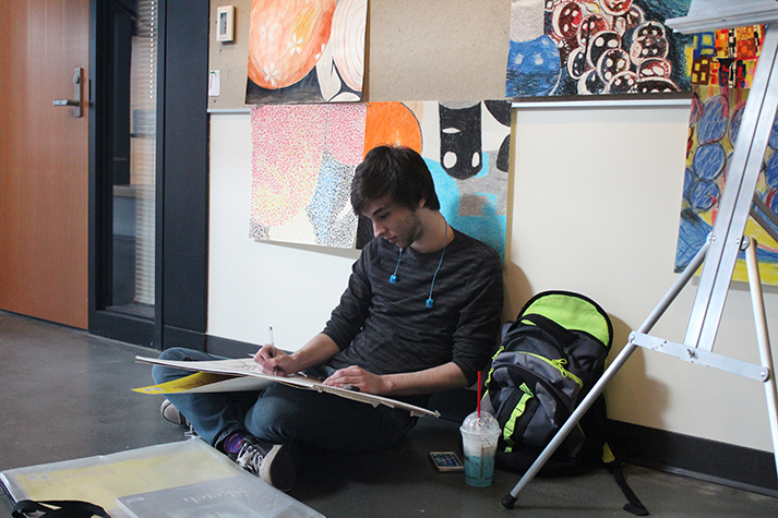 Jacob Mannon, a 19-year-old student at EvCC, listens to Take Cover by All Time Low as he draws quietly on the floor of White Horse Hall. As he works on his project, his music “helps (him) focus and ignore surroundings.”

“(It’s) one of my favorite tracks,” says Mannon. Listen to it here: https://www.youtube.com/watch?v=3XjElTw6FJc