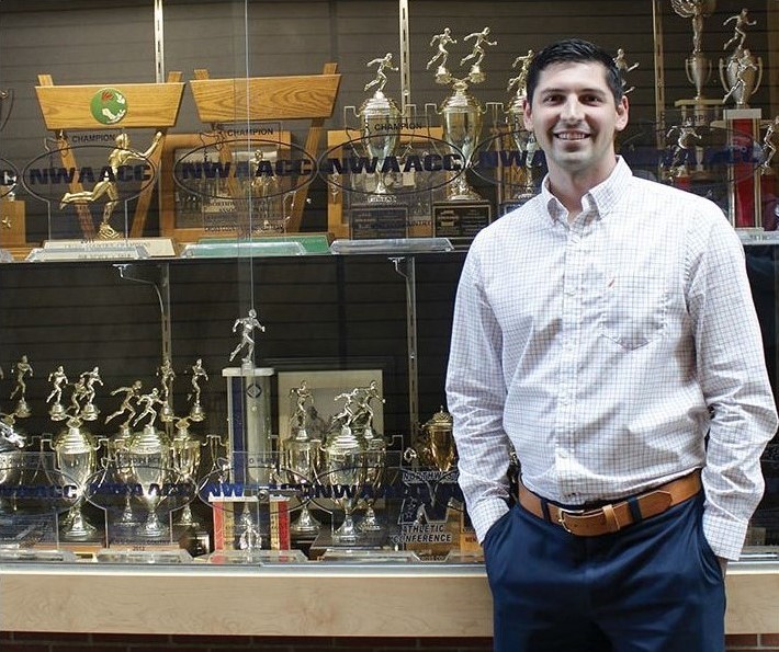 Garet Studer, EvCC's Athletic Director, poses in front of the fitness center's trophy case.